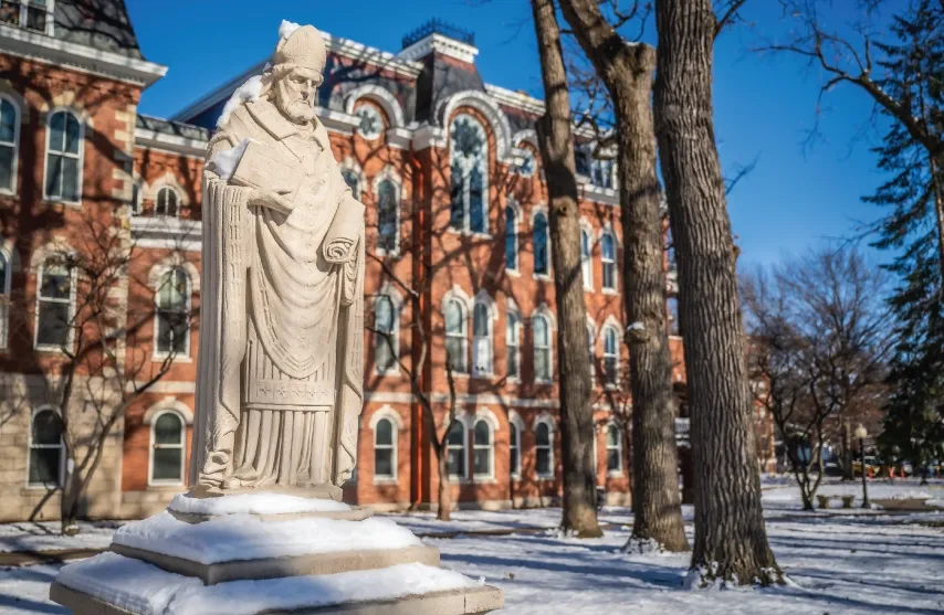 A stone statue of Saint Ambrose of Milan outside in the snow.